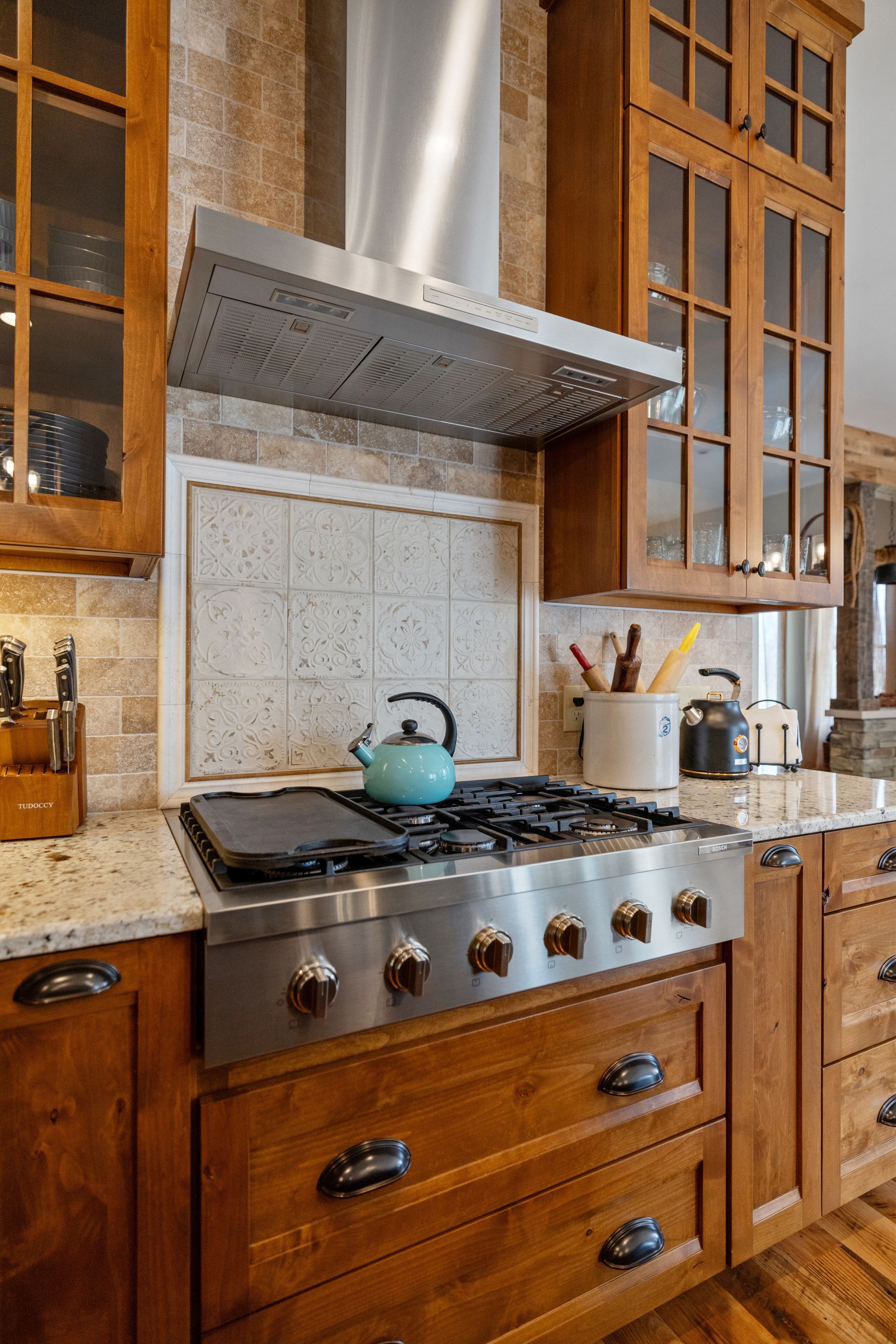 Kitchen with stainless steel range, teal kettle, and wooden cabinets.