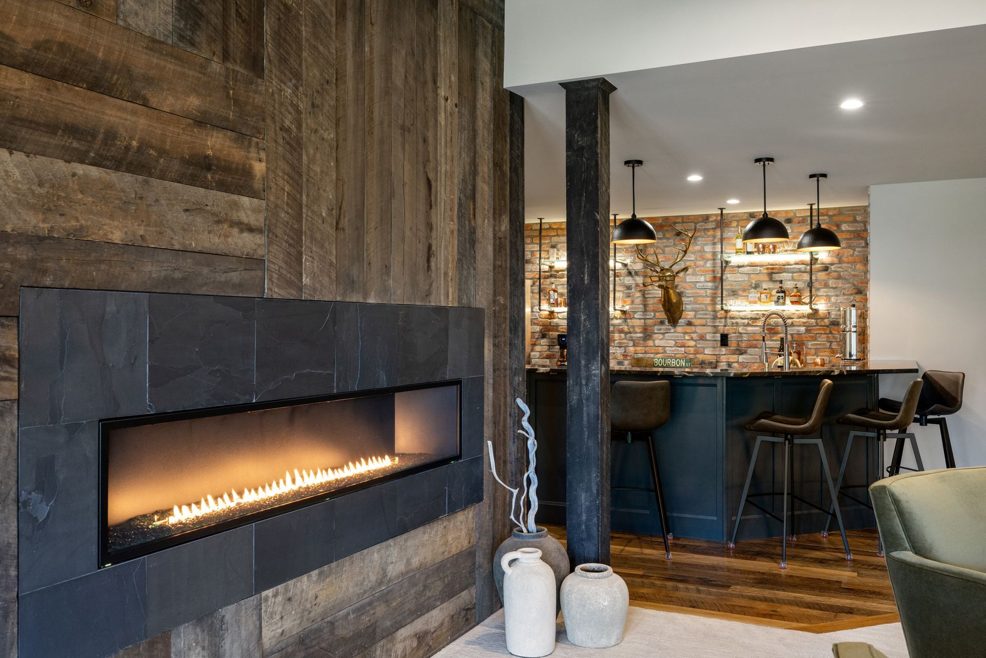 Fireplace in a rustic room with a bar in the background; wood walls, exposed brick, black accents.
