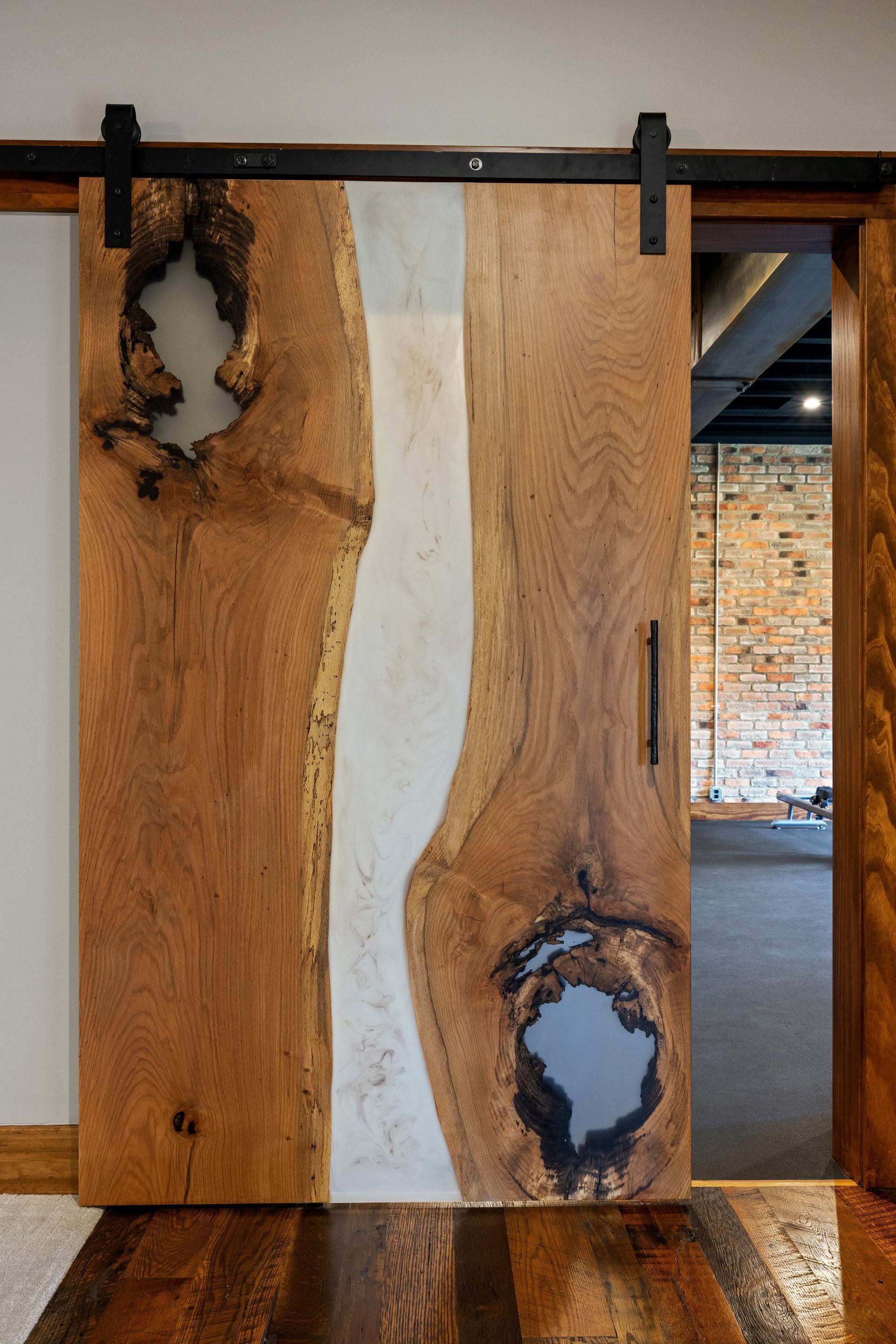 Barn door made of wood with a light-colored resin river down the center; the door has black hardware and a modern handle.