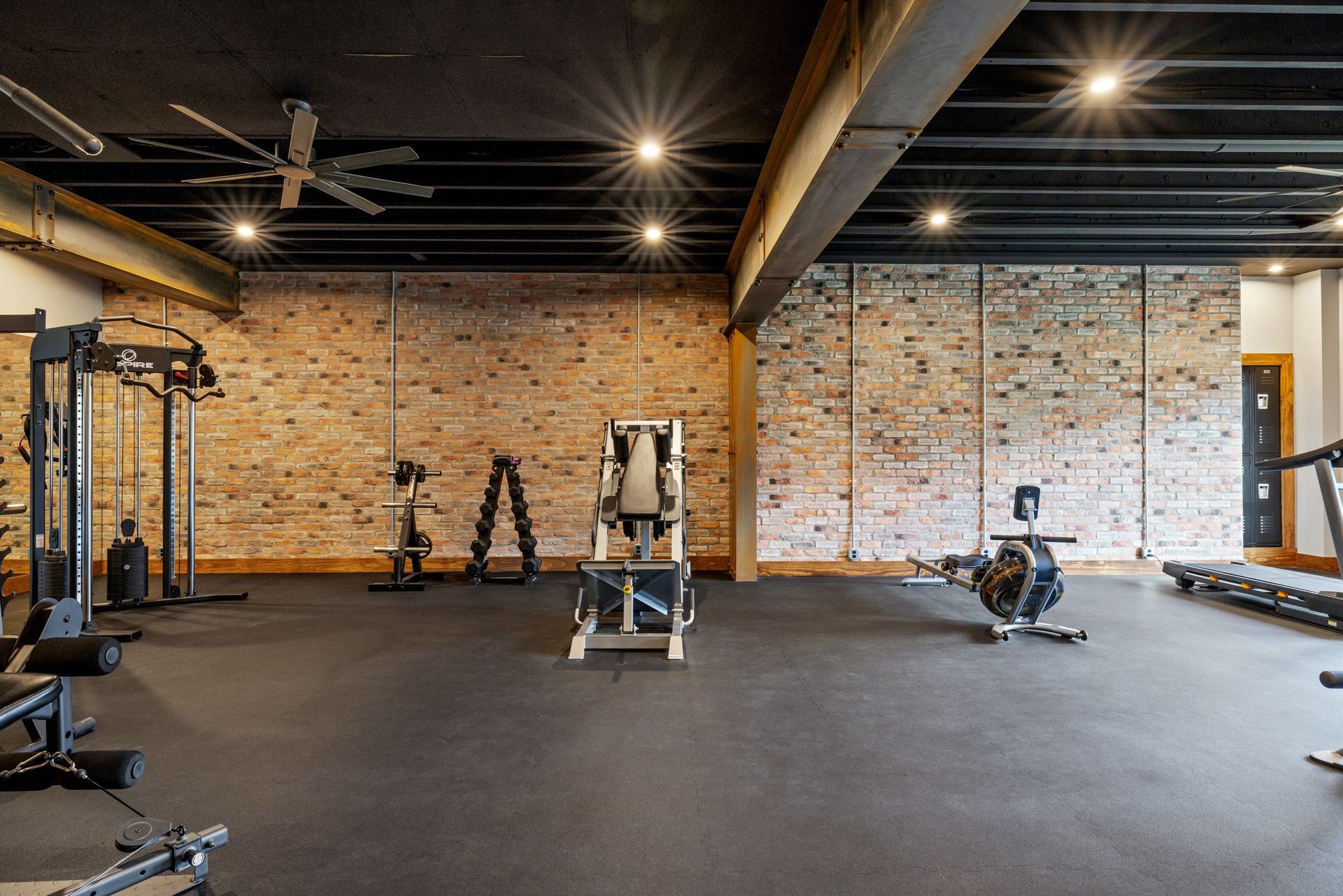 Gym interior with brick wall, black rubber flooring, and fitness equipment.