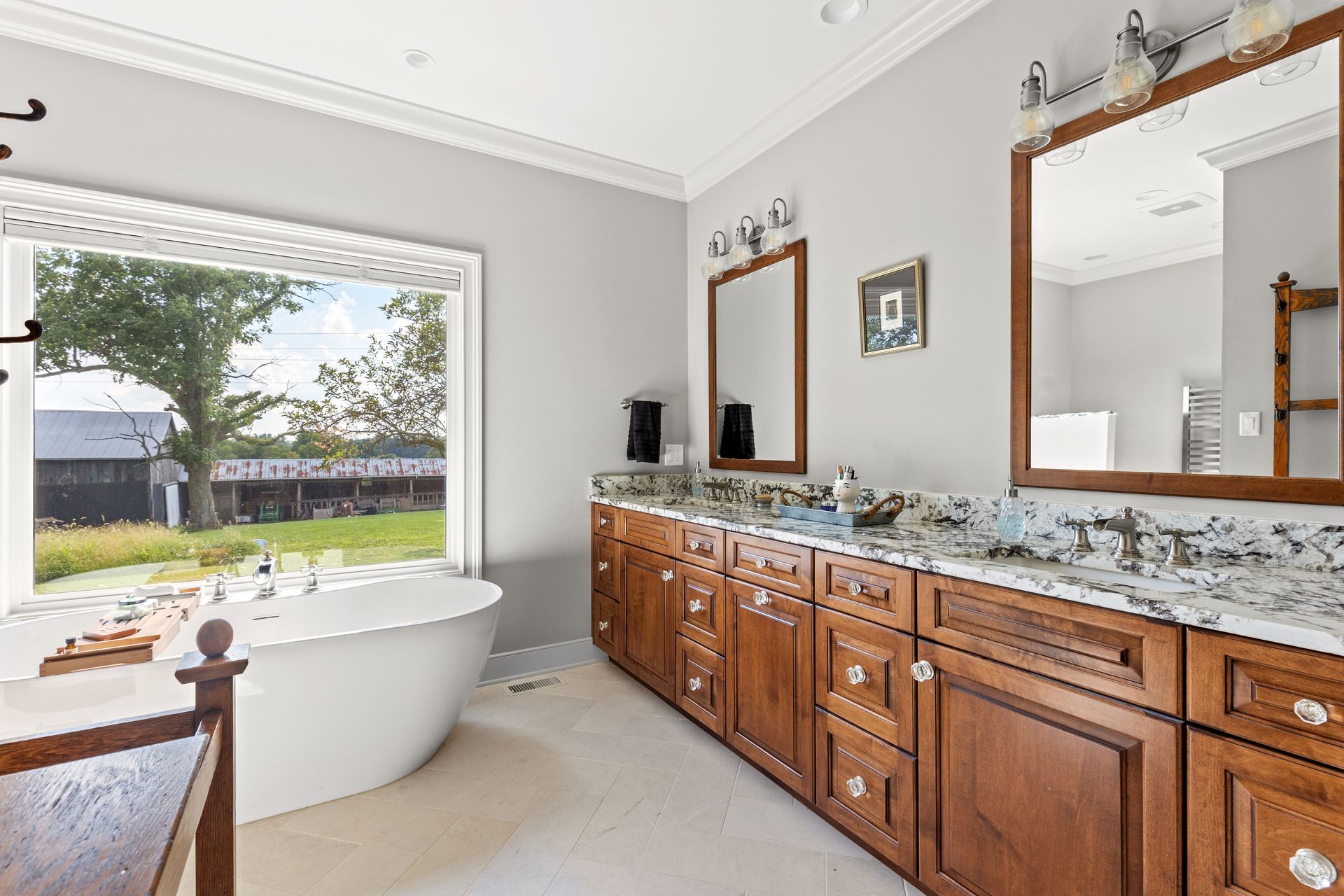 Bathroom with double vanity, soaking tub by a window, gray walls, and brown cabinets.