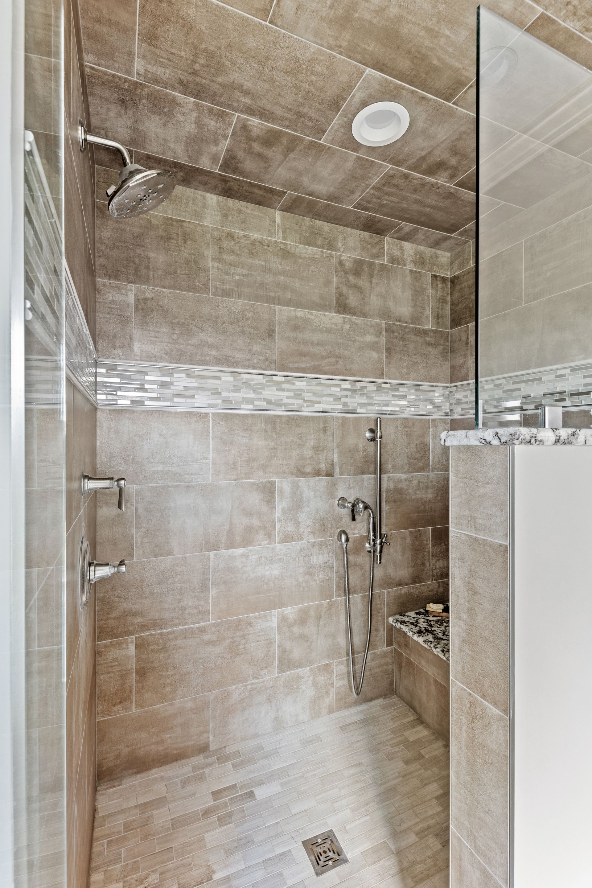 Modern beige tiled shower with glass doors, rain showerhead, and built-in bench.