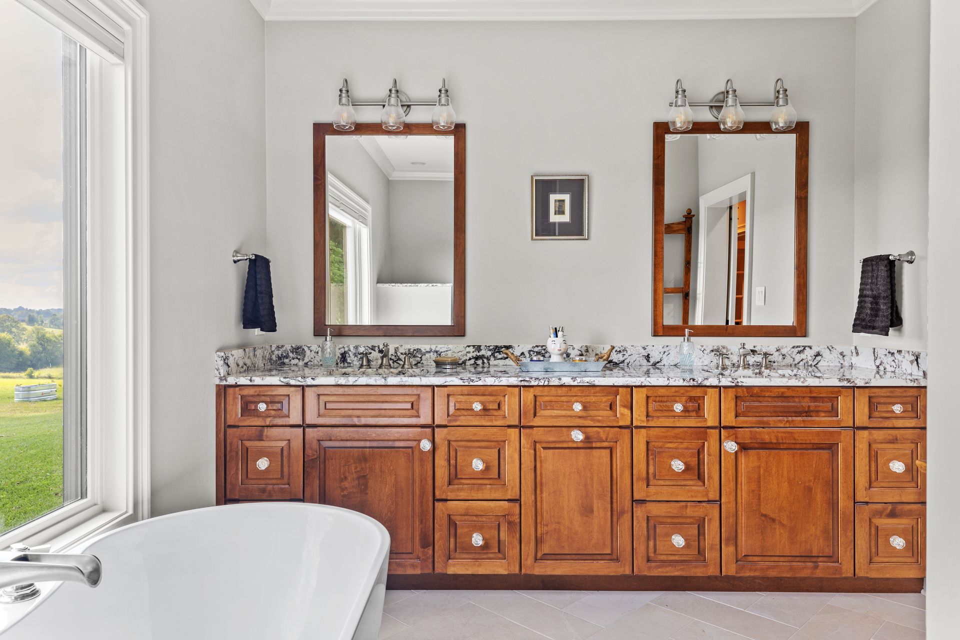 Bathroom with double sinks, wooden cabinets, framed mirrors, and a white tub.
