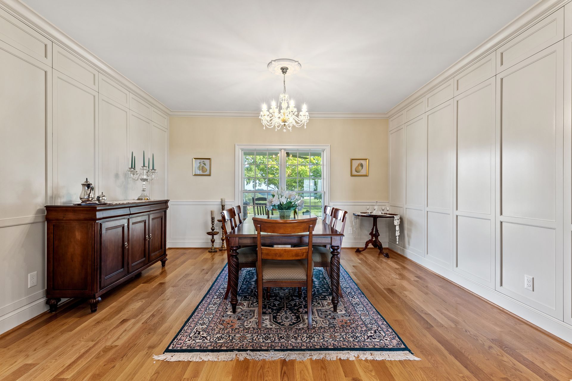 Dining room with a wooden table, chairs, rug, sideboard, and chandelier; paneled walls.