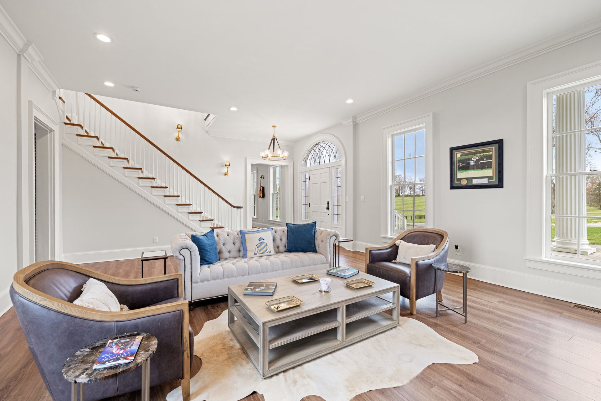 Living room with a staircase, sofa, armchairs, and a cowhide rug.