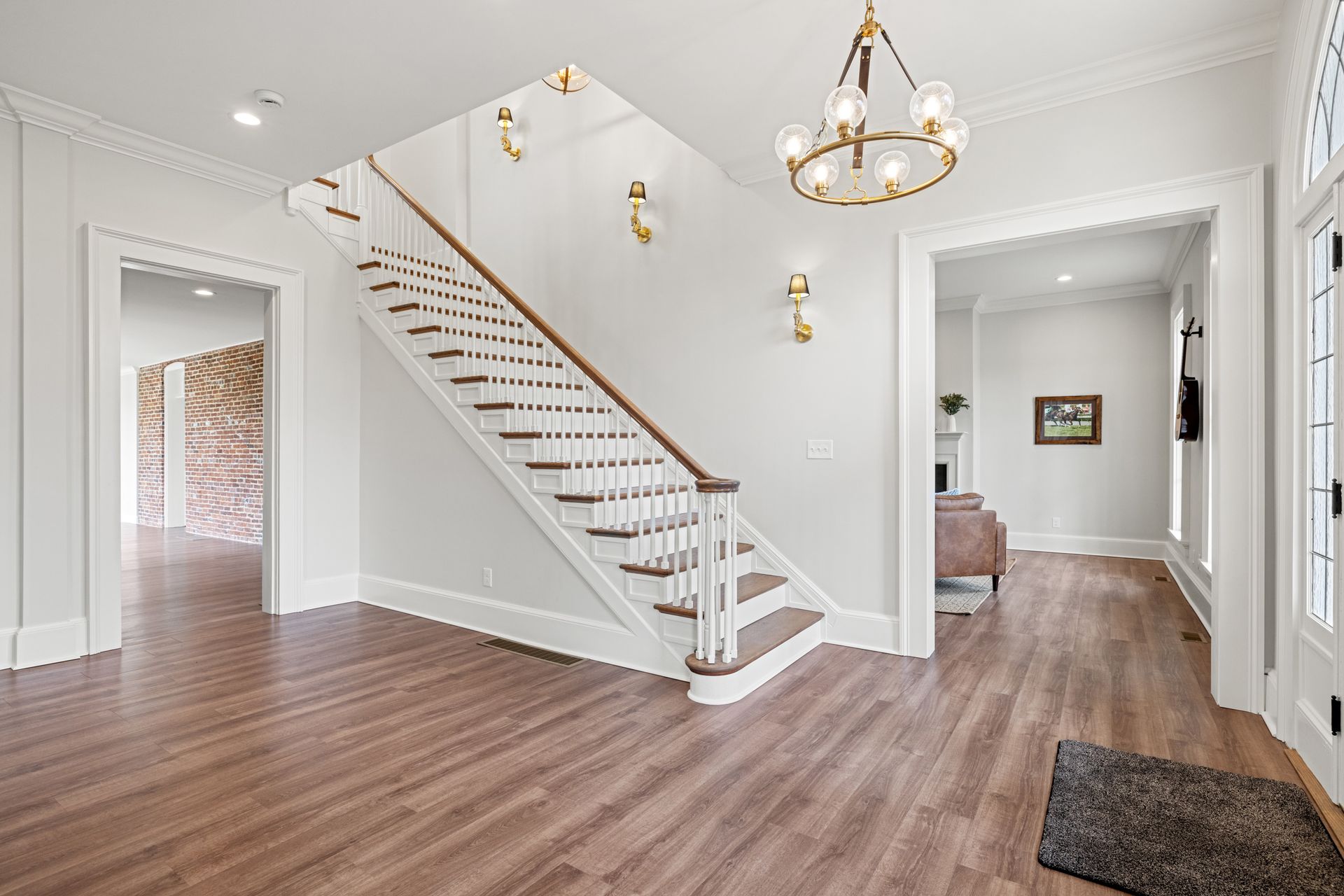 A bright entry hall with a staircase, hardwood floors, and two doorways.