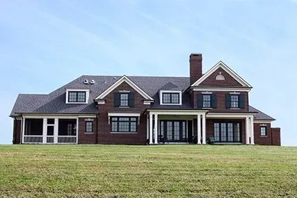 Large brick house with a dark gray roof, white columns, and black window frames.