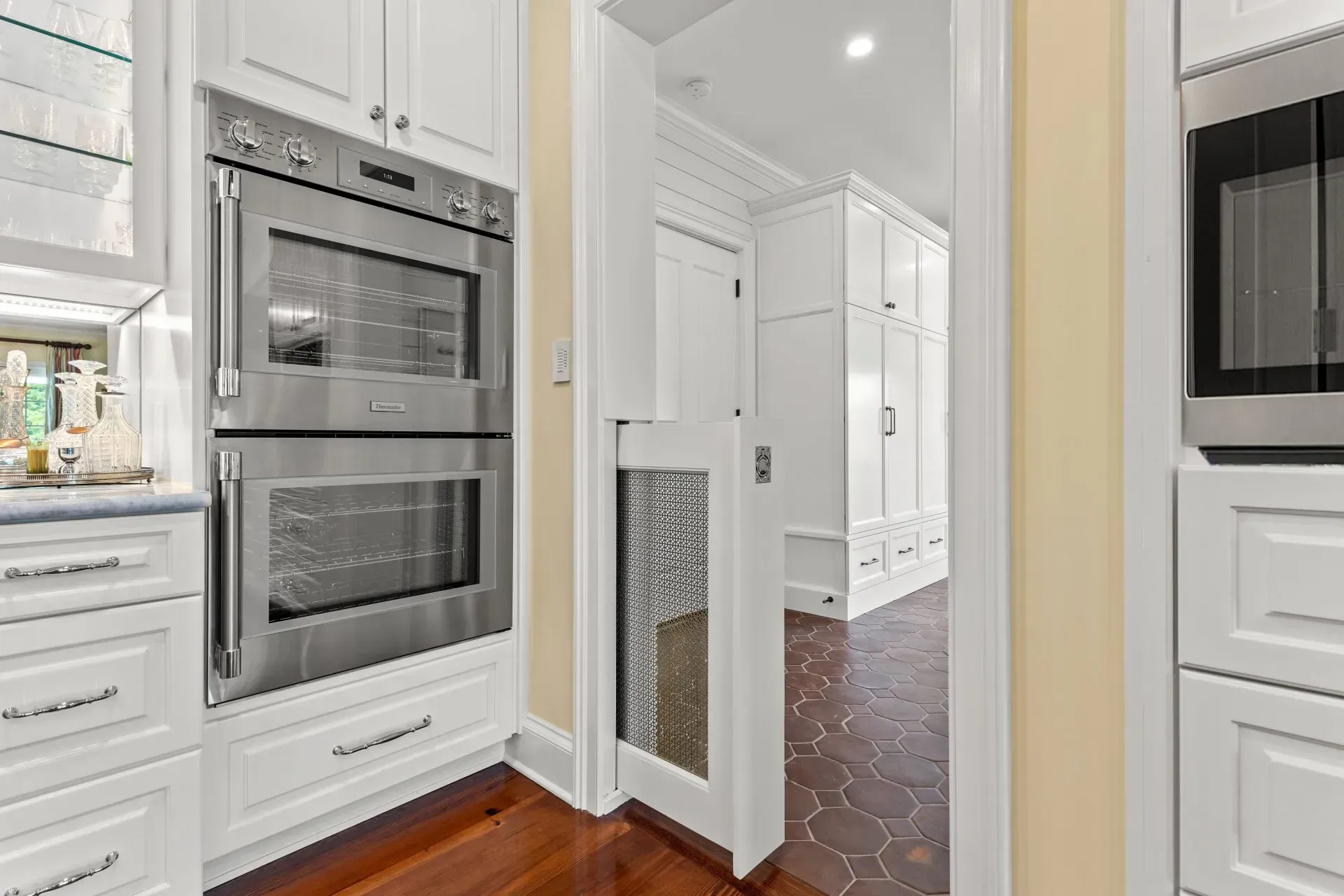 Kitchen with double ovens, doorway, and pantry with white cabinets.