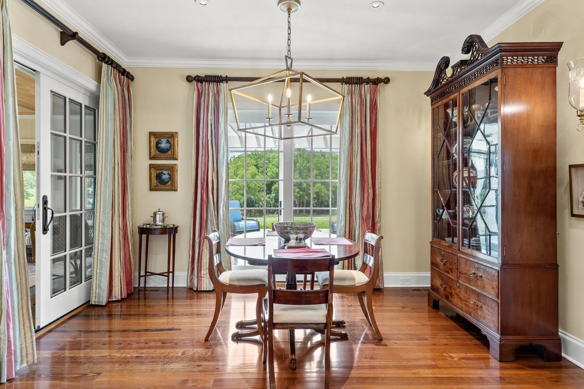 Elegant dining room with wooden table, chairs, hutch, and a large window overlooking a green yard.