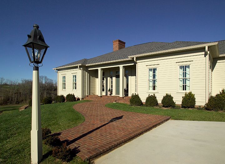 Brick pathway leads to a light beige house with a lamp post on the left, on a sunny day.