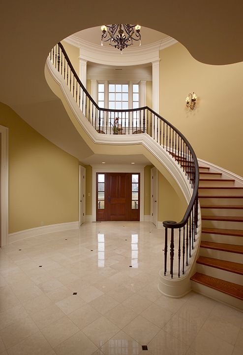 Grand foyer with curved staircase, brown door, marble floor, and yellow walls.