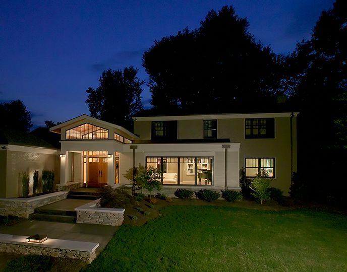 Two-story modern home at night with exterior lights illuminating the front yard and entrance.