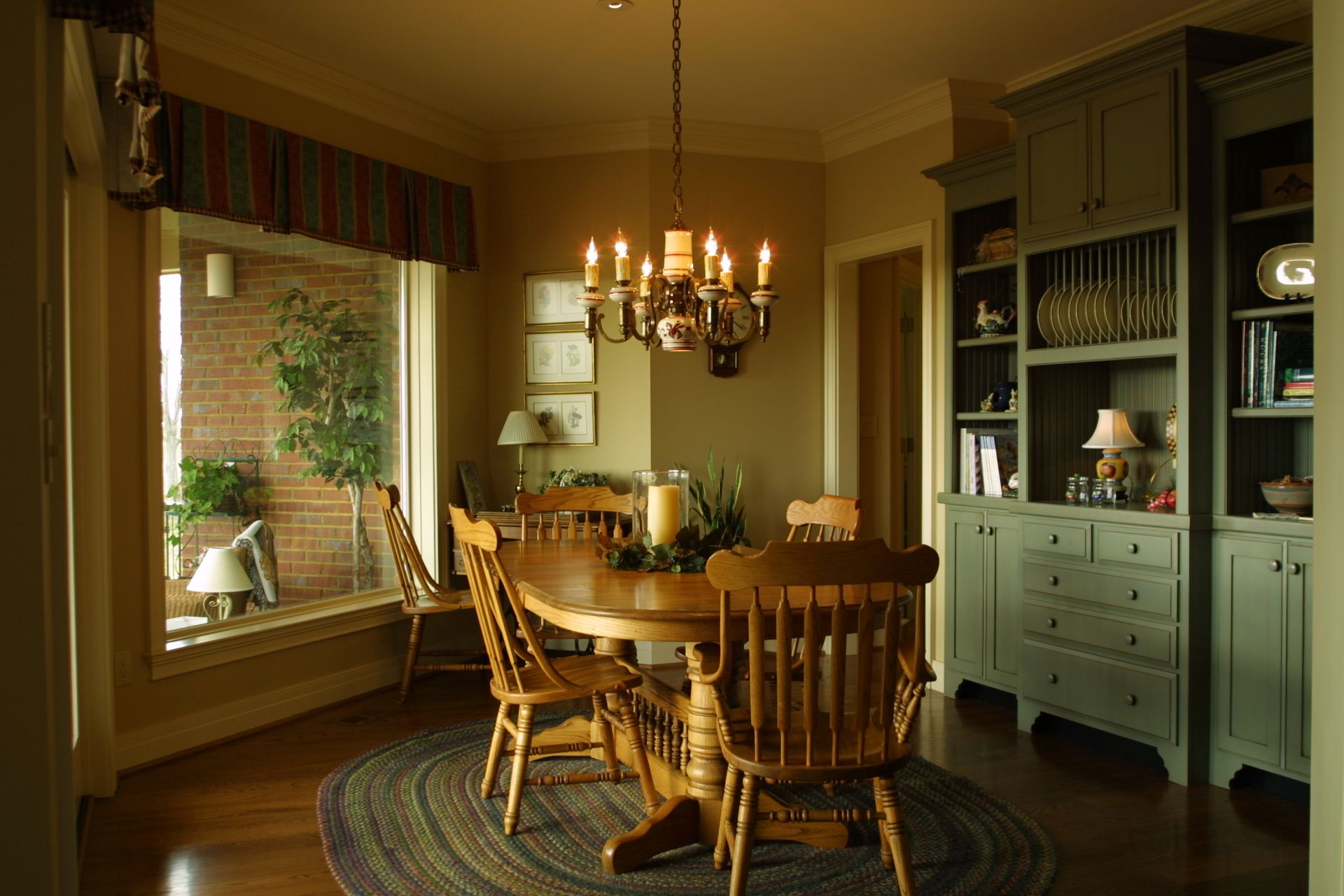 Dining room with round wooden table, chairs, chandelier, and built-in green cabinets.
