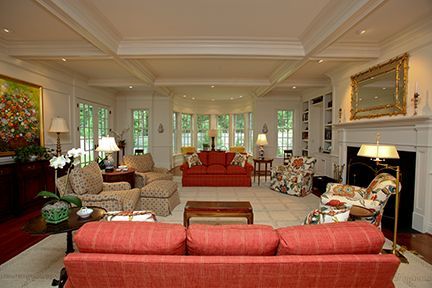 Spacious living room with various seating, fireplace, and windows.  Red and patterned fabrics with a white ceiling.