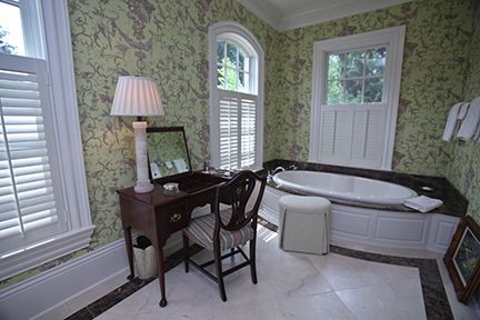 A bathroom with a vanity, bathtub, and two windows with shutters. Green floral wallpaper.