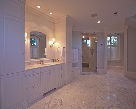 Spacious white bathroom with marble floor, glass shower, and vanity.