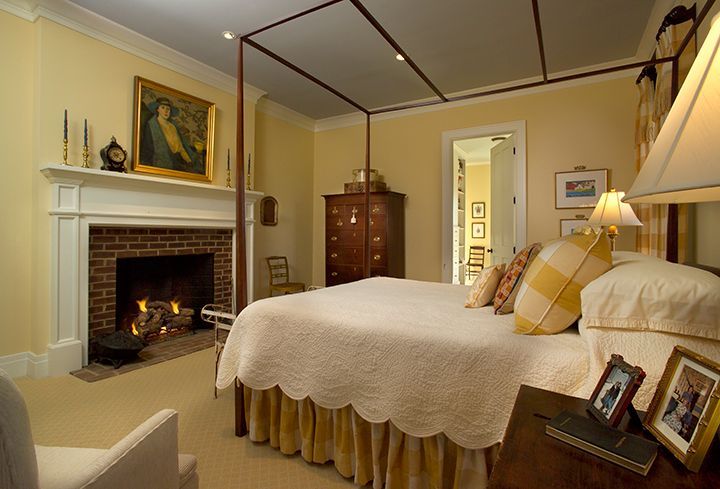 Bedroom with canopy bed, fireplace, and yellow accents.
