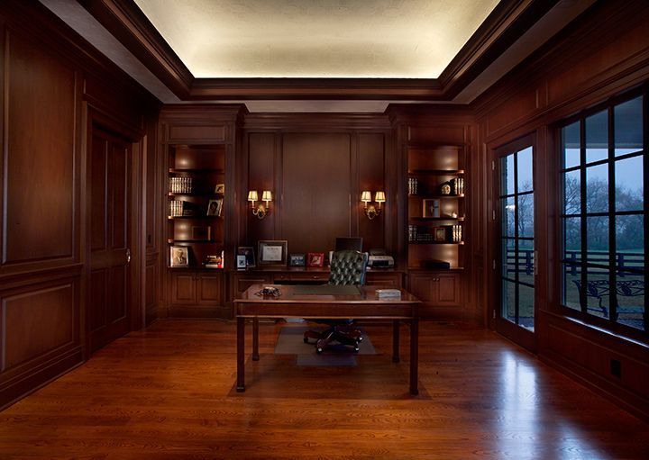 Dark wood-paneled office with desk, bookshelves, and large window overlooking a field.