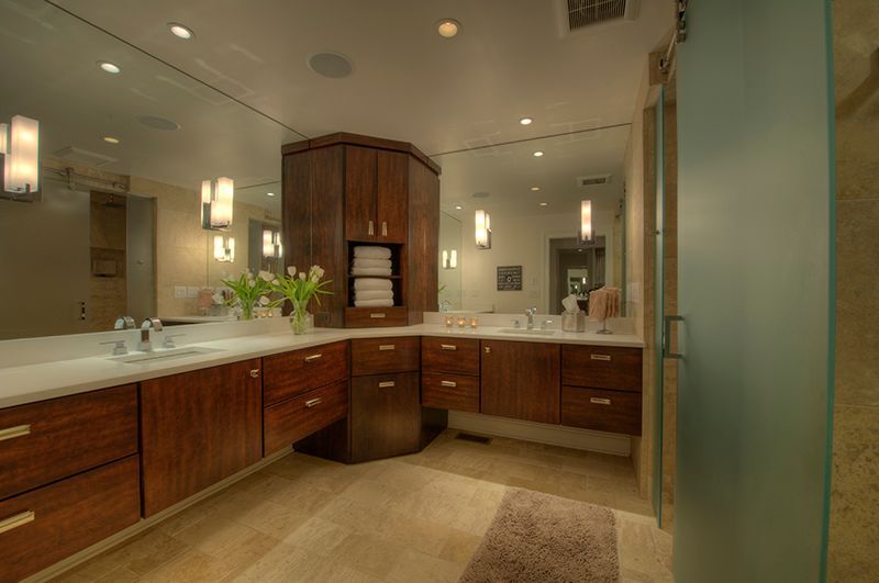 Bathroom with brown cabinets, large mirror, beige tile, and a frosted glass shower door.