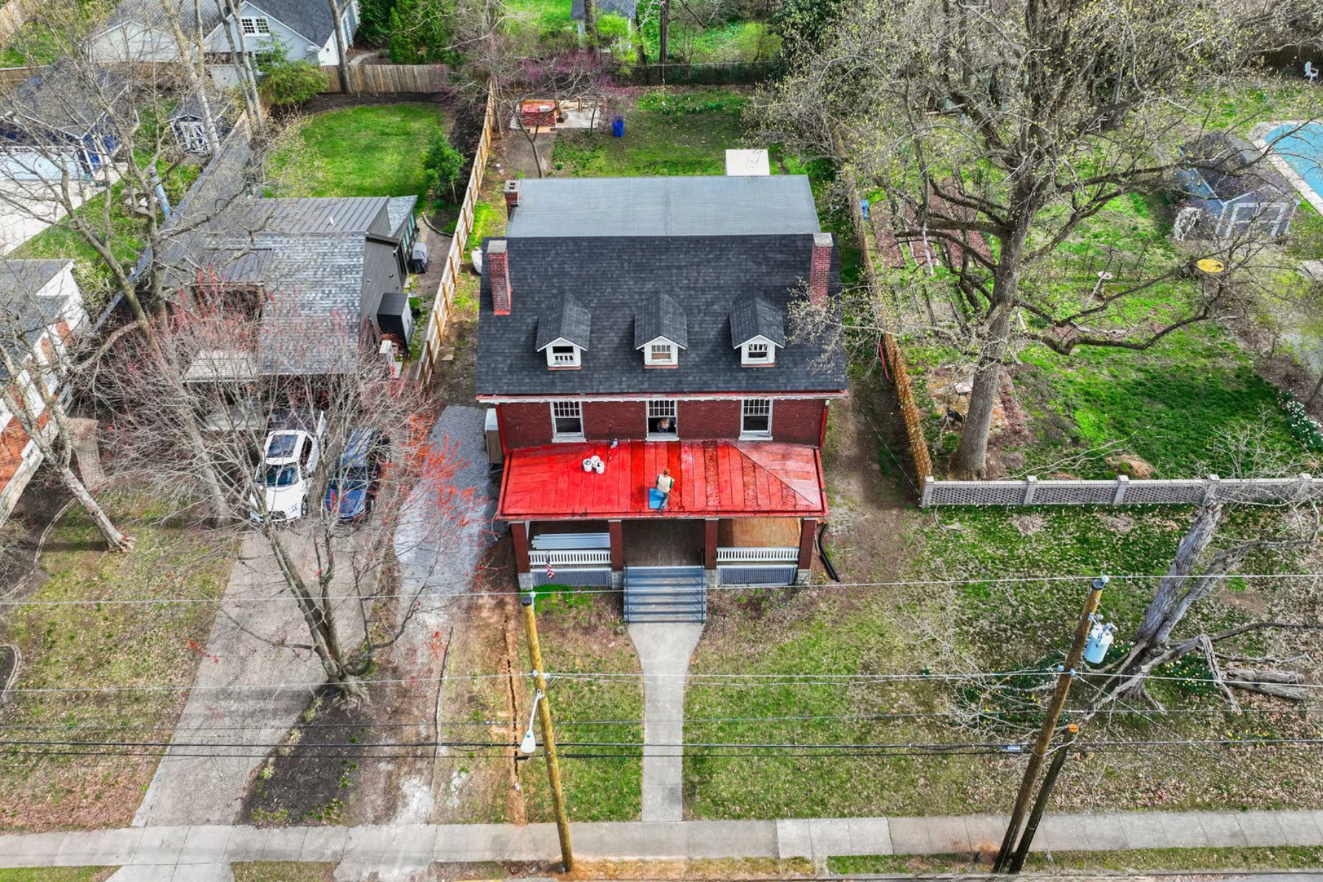 Aerial view of a brick home with a red porch, located in a residential neighborhood with trees and a pool.