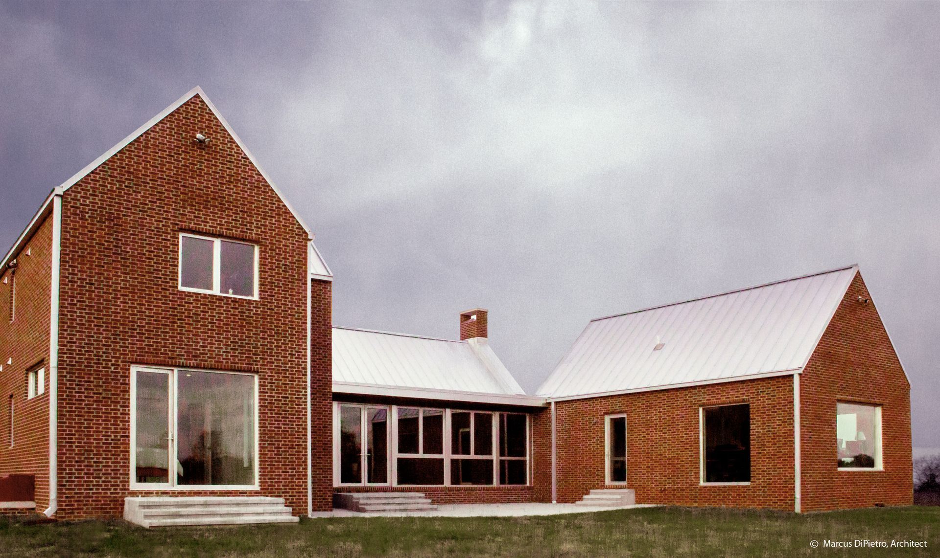 Brick home with gabled roofs, large windows, and metal roofing on a cloudy day.
