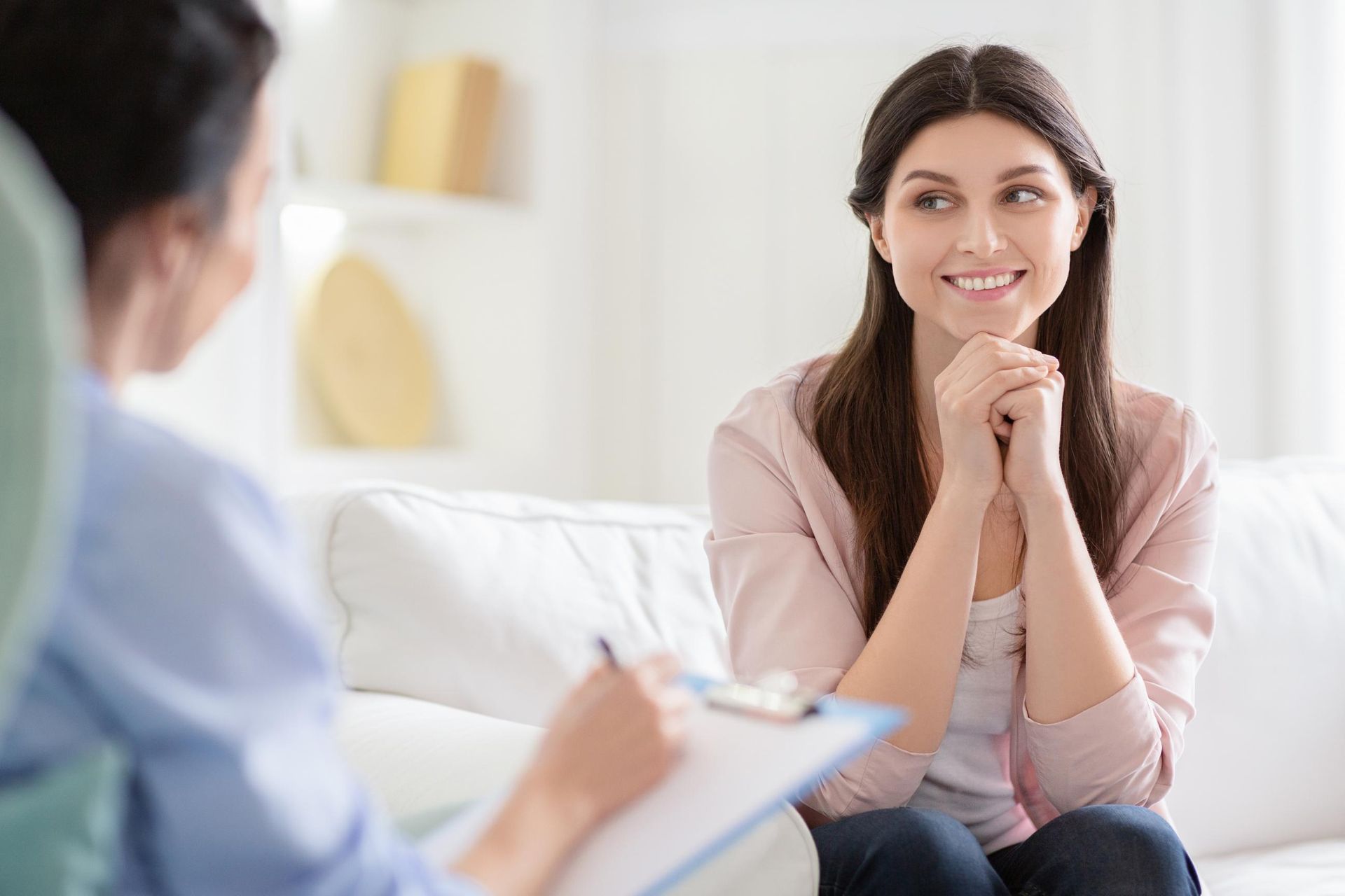 Woman smiling during a counseling session, seated on a white couch across from a therapist.