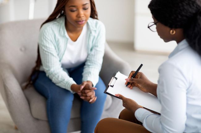 Counselor taking notes while talking with a seated client in a bright office