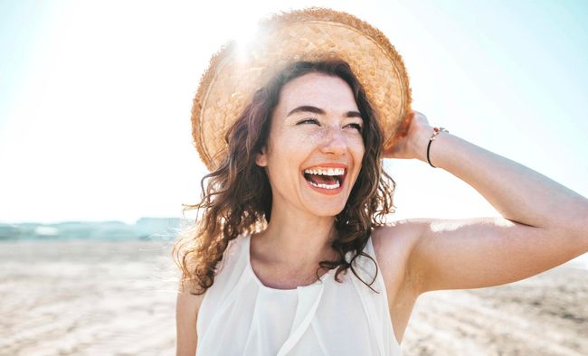 Smiling woman in a straw hat on a sunny beach with the sea in the background