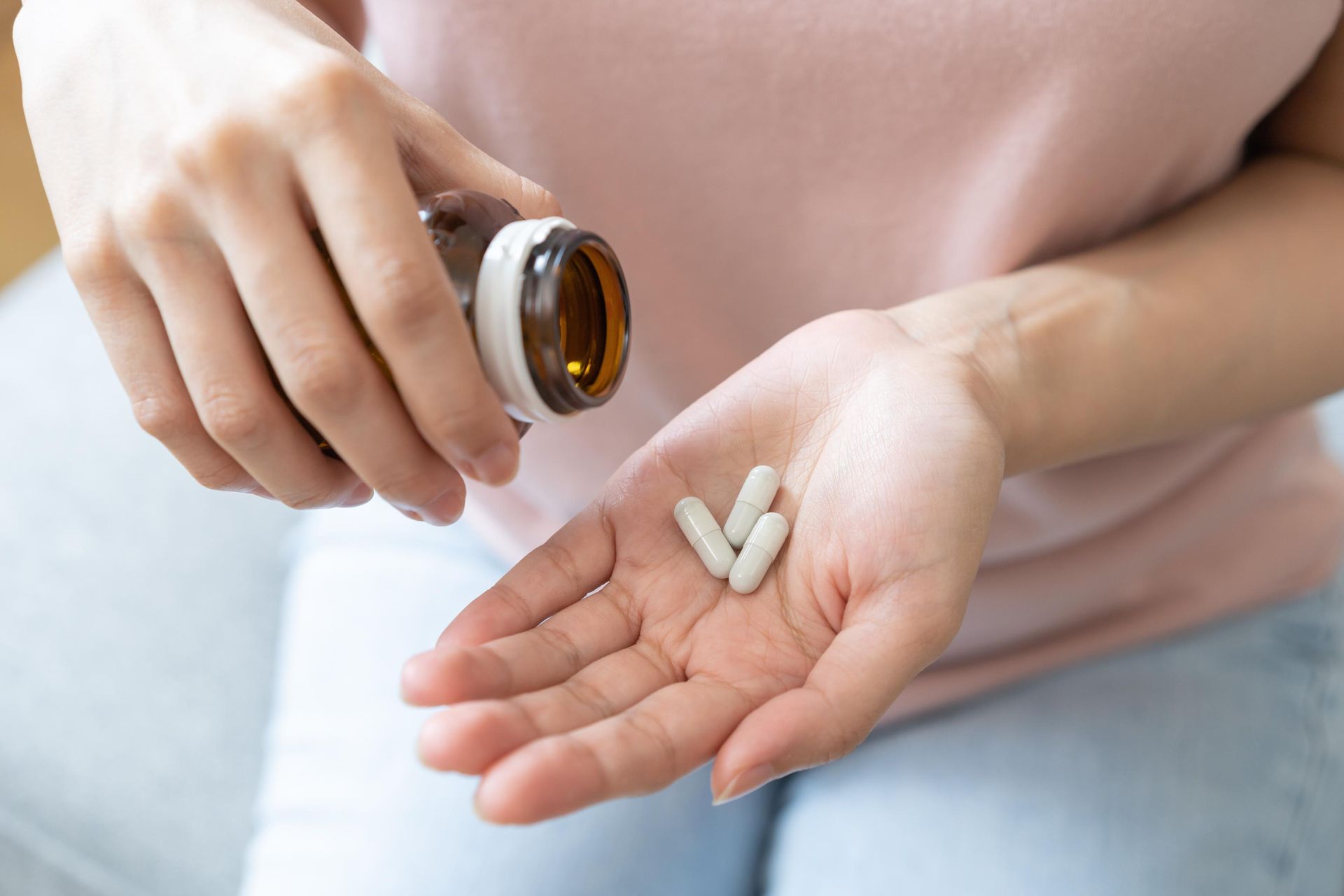 Hand pouring white pills from a brown bottle into an open palm