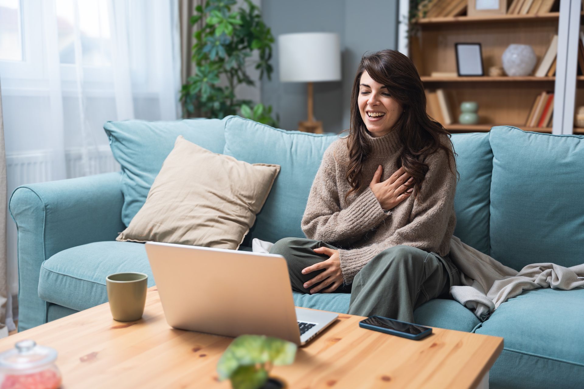 Woman smiling on a blue sofa with a laptop and coffee table in a bright living room