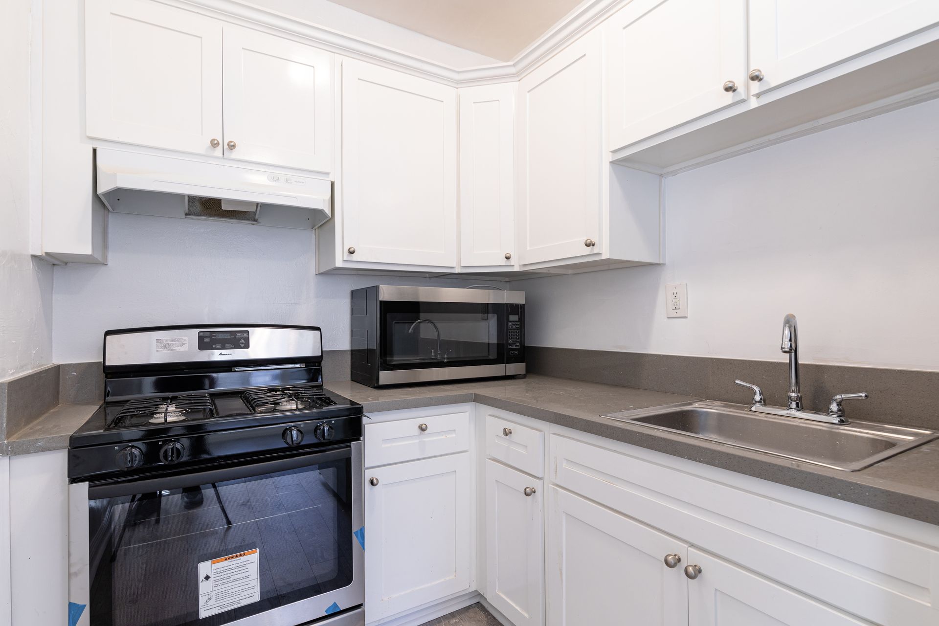 Small white kitchen with stainless steel appliances, grey countertops, and upper cabinets.
