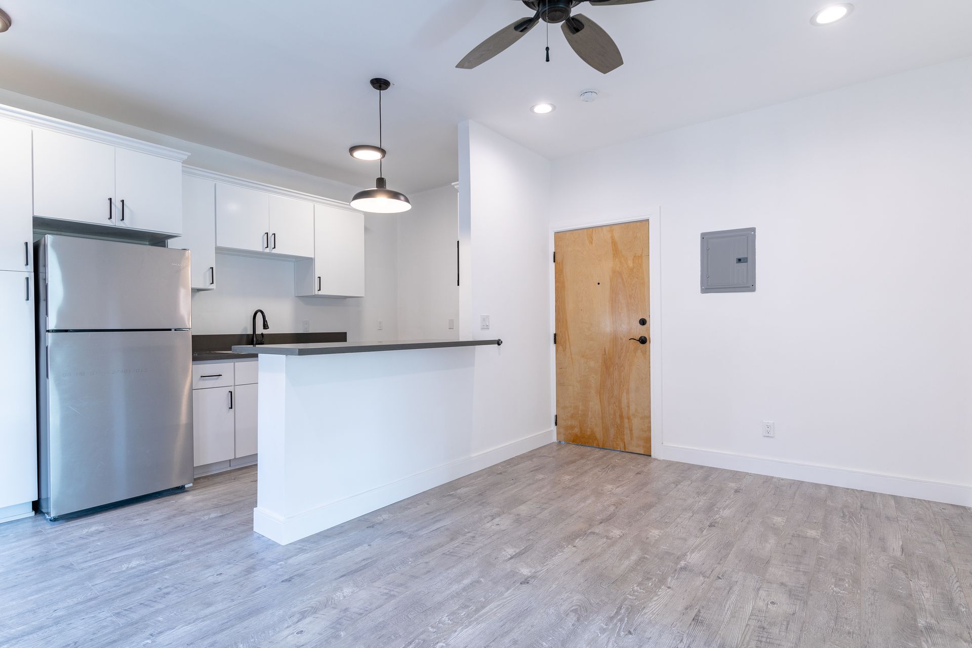 Interior view of a modern studio apartment with a kitchen, light wooden door, and gray flooring.