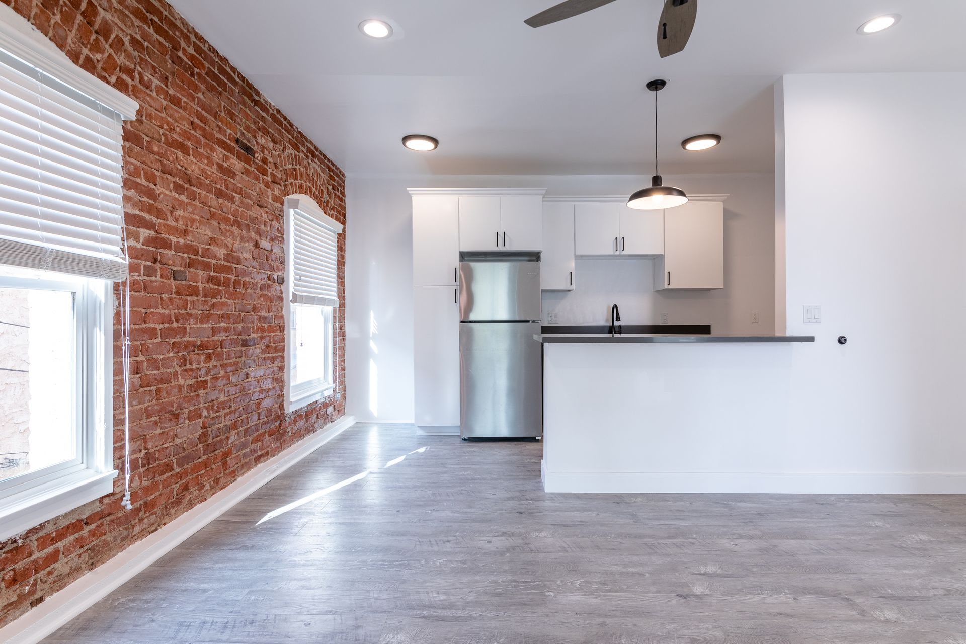 Interior view of an apartment with exposed brick wall, white kitchen cabinets, and stainless steel refrigerator.