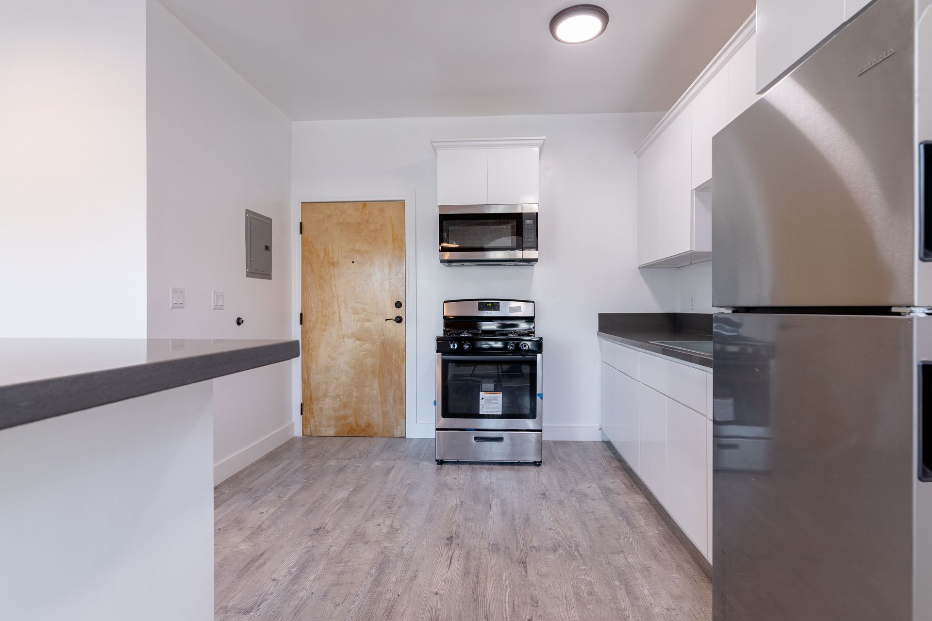 Modern kitchen with white cabinets, stainless steel appliances, and wood-grain floor.