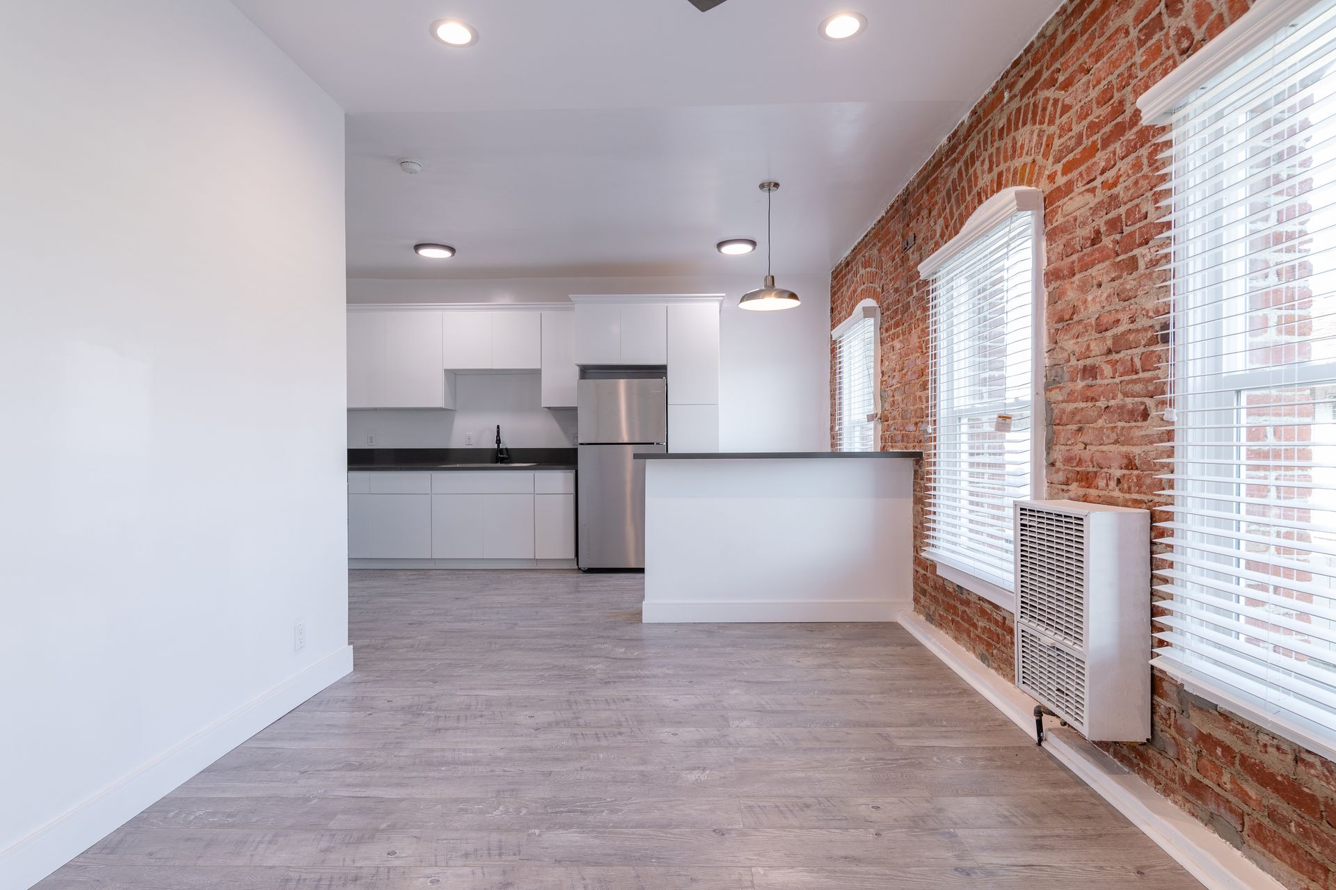 Interior of a modern apartment with exposed brick wall, white kitchen and trim, and concrete flooring.