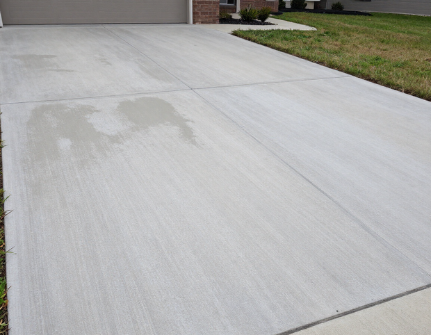 Concrete driveway with a large wet patch near the garage and lawn edge
