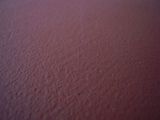 Primo piano di una superficie ruvida di una parete dipinta di color bordeaux scuro o rosso-brunastro.