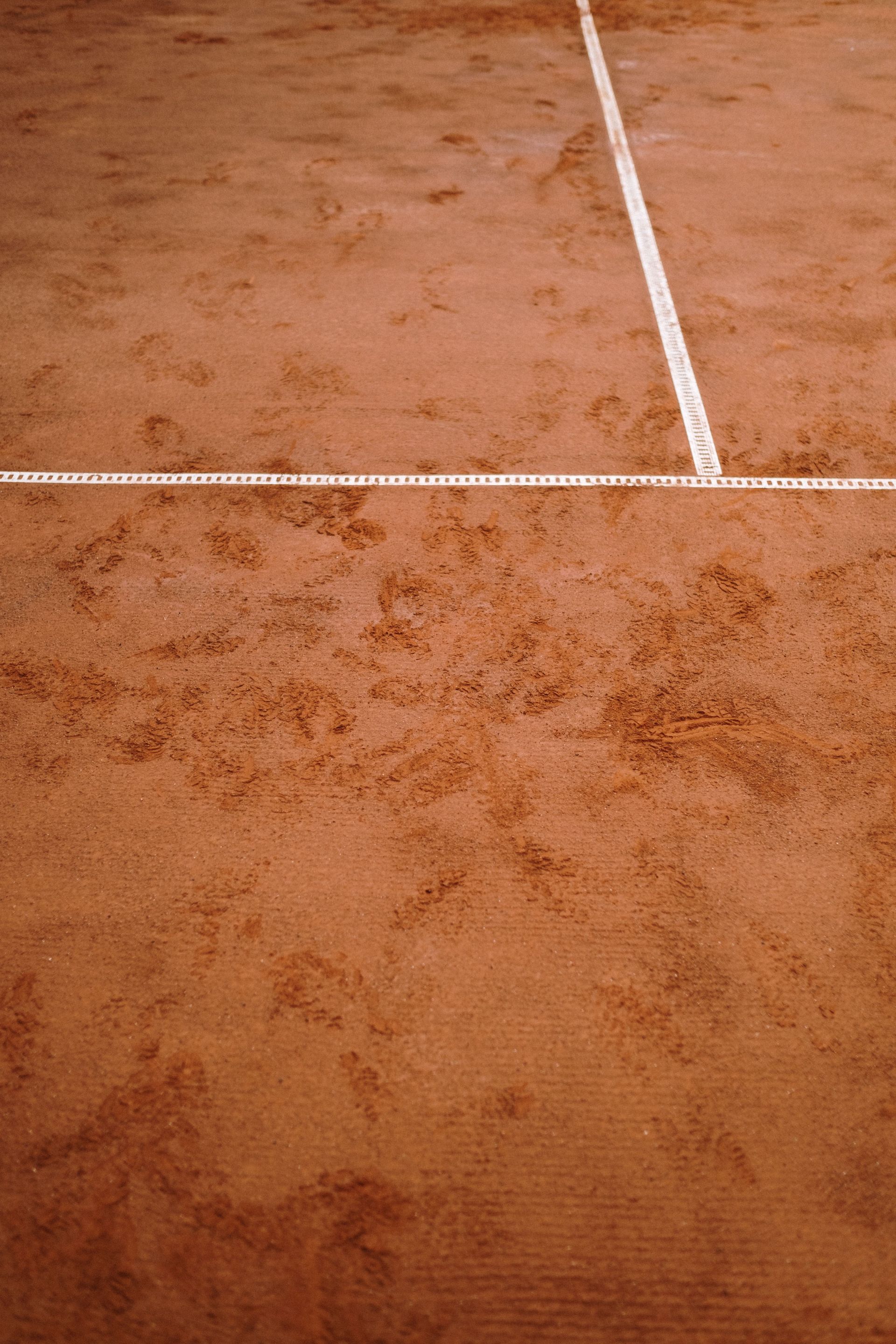 Una persona utilizza un tappeto di livellamento appesantito per spianare e uniformare la superficie di un campo da tennis in terra battuta rossa.
