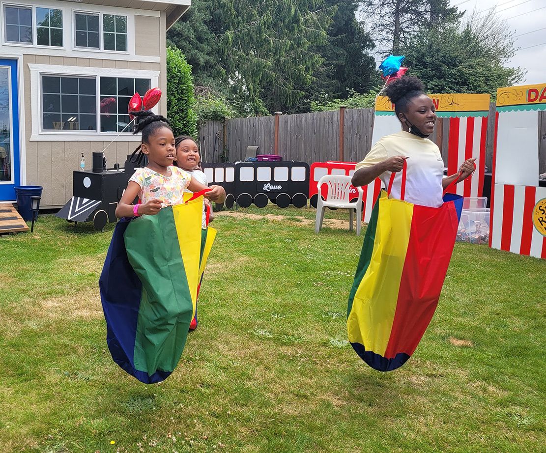 Two young girls are jumping sacks in a yard.