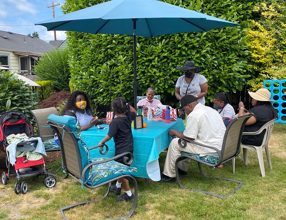 A group of people are sitting around a table under an umbrella in a backyard.