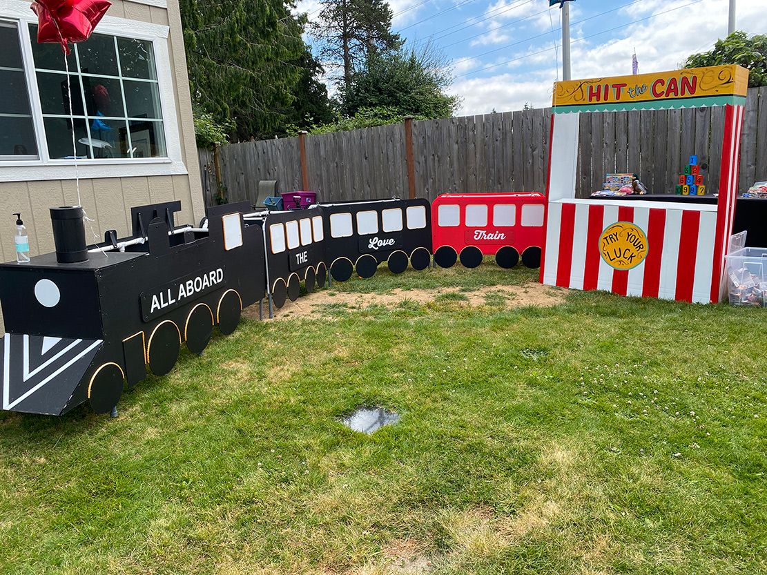 A train is sitting in the grass next to a carnival booth.