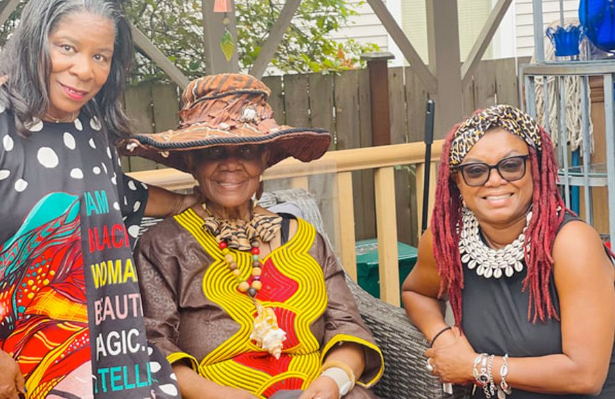 Three women are sitting next to each other on a porch . one of the women is wearing a hat.