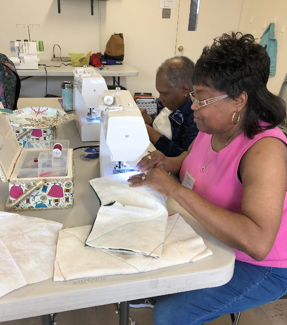 A woman in a pink shirt is sitting at a table using a sewing machine.