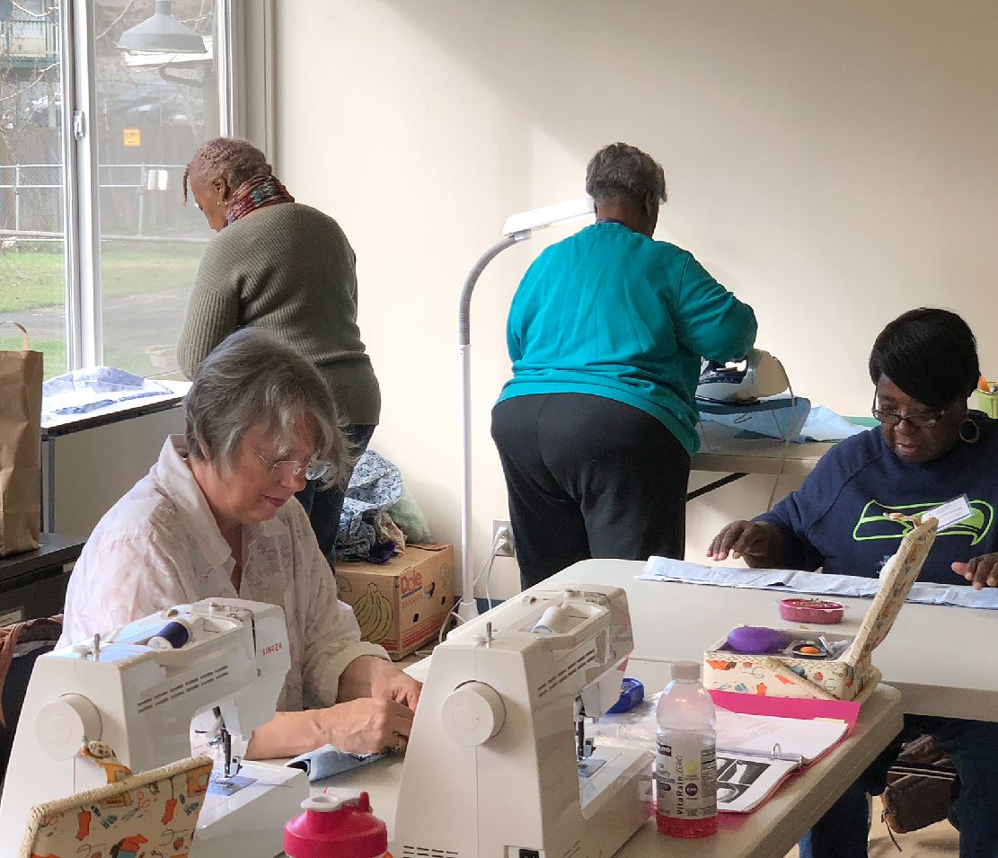 A group of people are sitting at a table using sewing machines.
