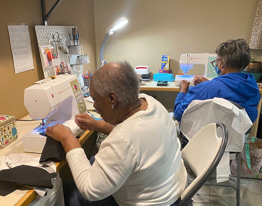 Two people are sitting at a table using sewing machines.