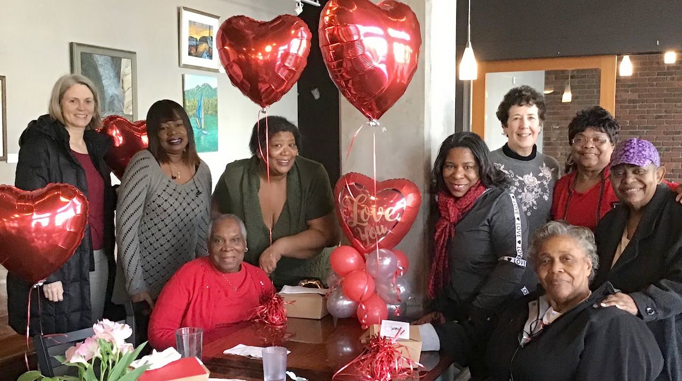 A group of people are sitting around a table with balloons in the shape of hearts.