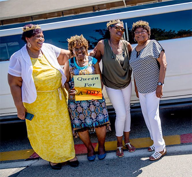 A group of women standing in front of a bus holding a sign that says queen for a day