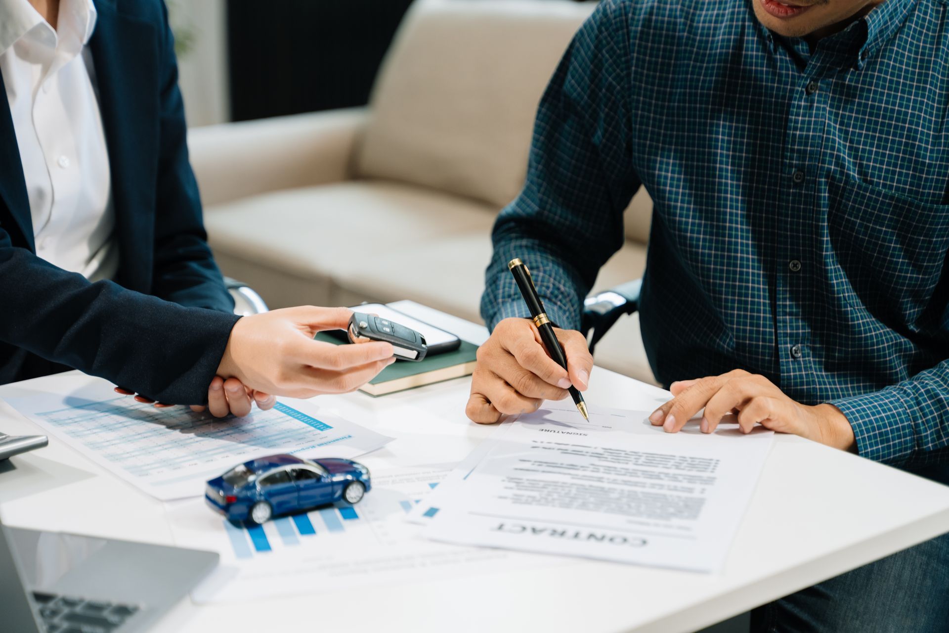 Two people signing documents at a white table with a calculator and blue car model