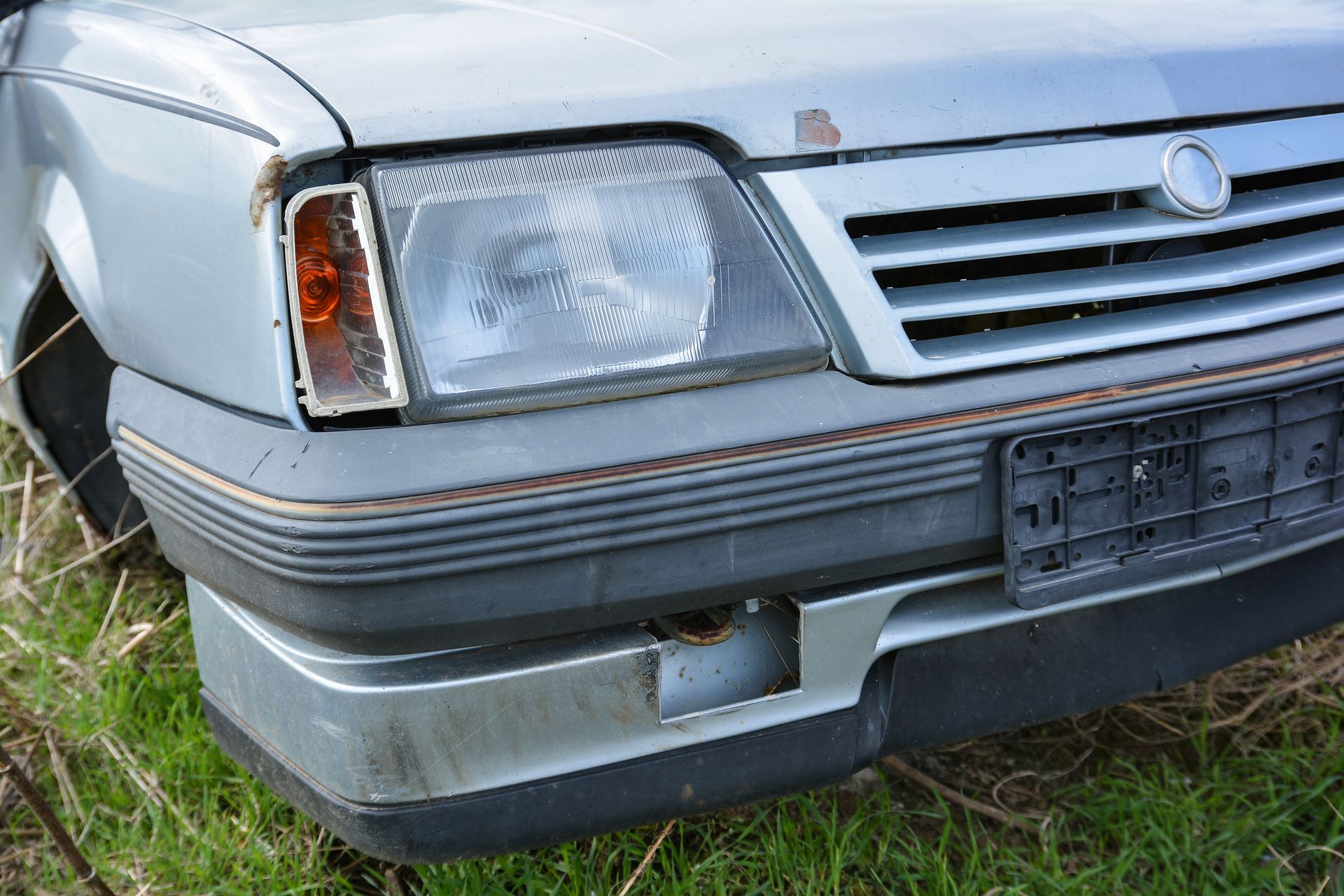 Close-up of a damaged silver car front bumper and headlight in grassy outdoor area Close-up of a damaged silver car front bumper and headlight in grassy outdoor area