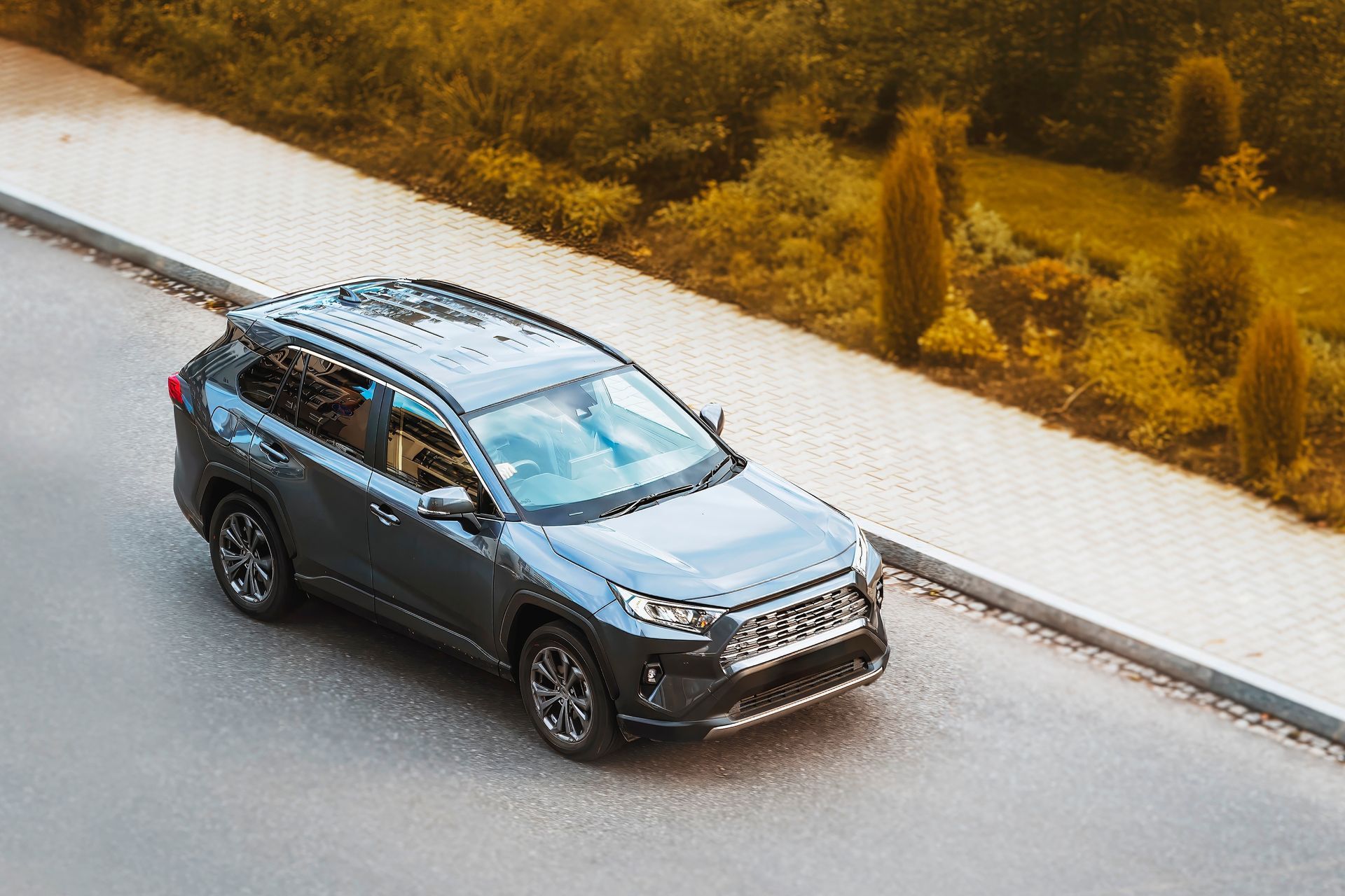 Gray SUV driving on a road beside a sidewalk and grassy embankment